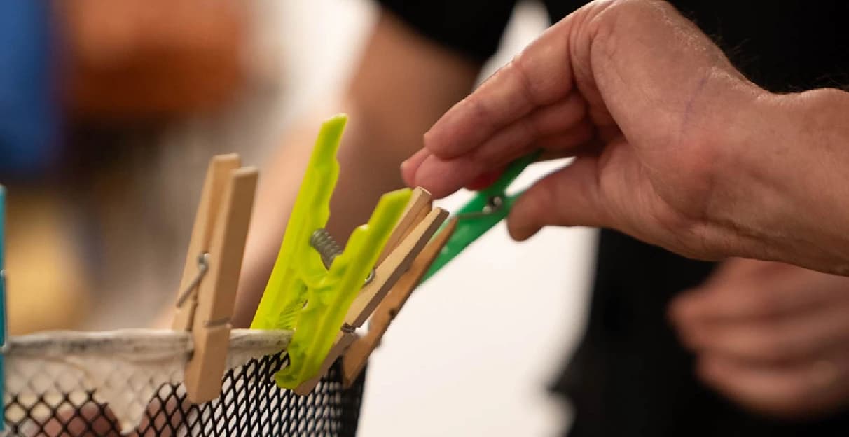 Mano colocando pinzas en una cesta durante un ejercicio de motricidad fina.