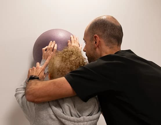 Imagen de un fisioterapeuta ayudando a una mujer a realizar un ejercicio con una pelota.